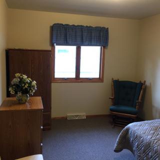 A simple bedroom with a dresser, chair, and window.