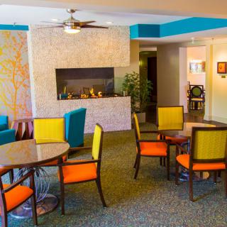 A modern and colorful seating area featuring tables, vibrant chairs, and a fireplace.