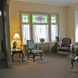 A cozy living room with stained glass windows, featuring armchairs and a side table with a lamp.