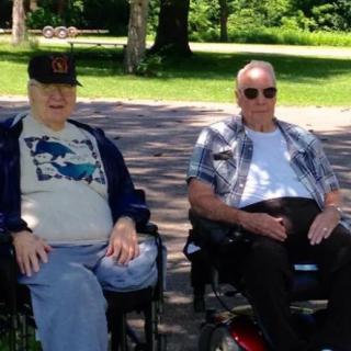 Two men sitting in wheelchairs enjoying a sunny day in the park.