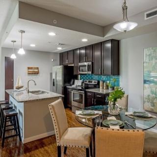 A modern kitchen with an open floor plan, featuring a dining area, island with bar stools, and stainless steel appliances.