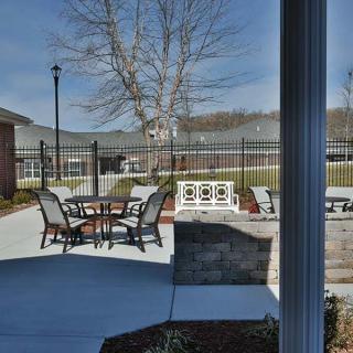 A serene outdoor patio area with tables and chairs, surrounded by a fence and trees.