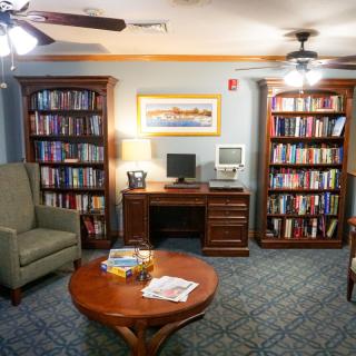 A cozy library reading area featuring bookshelves, a computer desk, armchair, and coffee table.