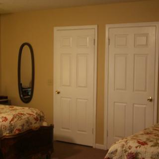A cozy bedroom featuring two beds with floral bedding, a wall-mounted mirror, and two white doors.