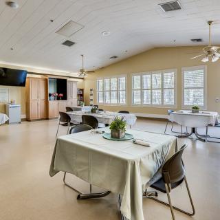 A spacious dining area with neatly arranged tables and chairs, featuring large windows and ceiling fans.
