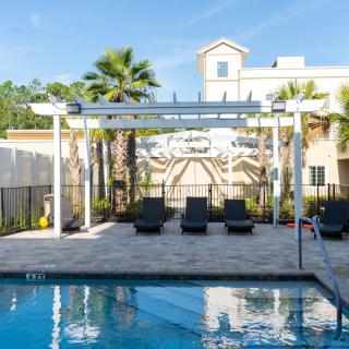 A serene outdoor swimming pool area with lounge chairs and a pergola, surrounded by palm trees on a sunny day.