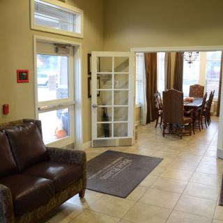 A comfortable lobby area featuring leather chairs, a table with chairs in the background, and natural lighting from large windows.