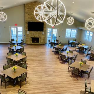A spacious dining area with multiple tables and modern pendant lighting, featuring a central fireplace.