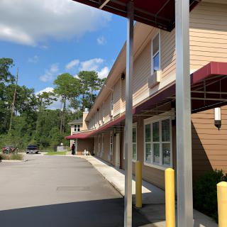 A view of a building with an awning and a nearby parking lot on a sunny day.