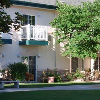 A residential building with a balcony, surrounded by trees and a well-kept lawn.