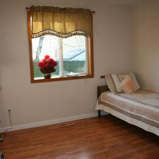 A minimalist bedroom with a single bed, a window adorned with curtains, and a flower pot on the sill.
