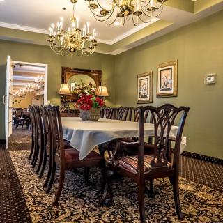 An elegant dining room with a large wooden table, surrounded by chairs and adorned with a chandelier.