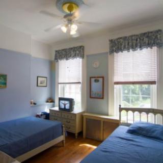 A cozy bedroom with twin beds, a ceiling fan, and ample natural light from two windows.