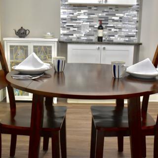 A cozy dining area with a round wooden table set for two, featuring elegant place settings and a stylish kitchen backdrop.