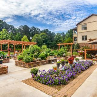 A beautifully landscaped garden with various blooming flowers and plants, adjacent to a building on a sunny day.