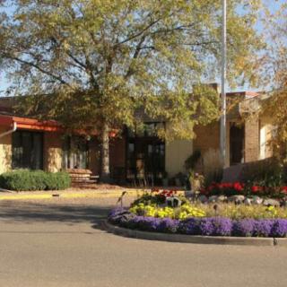 The entrance of a building surrounded by landscaped gardens and colorful flowers on a sunny day.