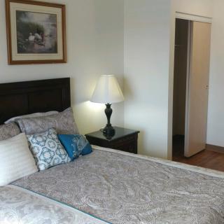 A cozy bedroom with a neatly made bed, decorative pillows, and a nightstand with a lamp.