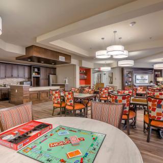 A cozy dining area with a Monopoly board game set up on a table, surrounded by colorful chairs and modern kitchen facilities.