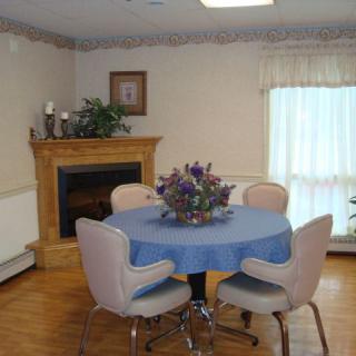 A cozy dining room with a round table, four chairs, and a fireplace.