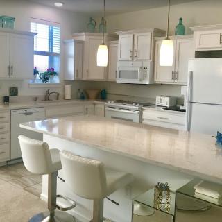A modern kitchen with white cabinets and an island counter, featuring bar stools and pendant lights.