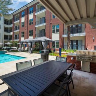An apartment complex with a swimming pool and outdoor seating area, featuring a grill station and balconies overlooking the pool.