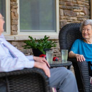 An elderly couple enjoys a relaxing conversation while seated on their porch.