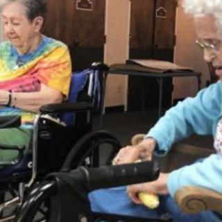 Two elderly individuals in wheelchairs inside a care facility.