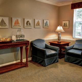 A cozy living room with two armchairs, a side table, and a lamp, adorned with decorative art on the walls.
