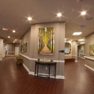 A well-lit hallway with wood flooring, featuring artwork and leading to a reception area.