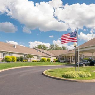 A building with an American flag in front and a clear blue sky with clouds above.