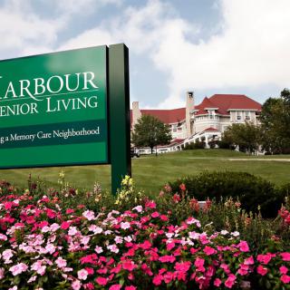 A scenic view of a senior living facility with colorful flowers and a welcoming sign.