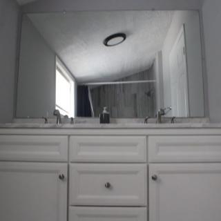 A bathroom with a large mirror above a double sink and white cabinet.