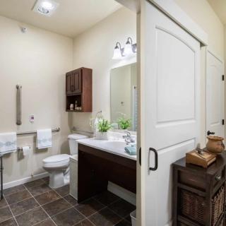 A modern bathroom featuring a sliding door, with a sink, mirror, and toilet, accented by tiled flooring and neatly arranged towels.