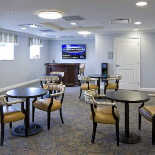 A modern meeting room with multiple tables and chairs, featuring a television on the wall.