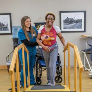 A healthcare professional assists a patient as she practices walking with the help of a walking aid.