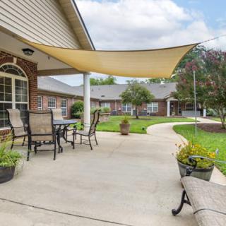 A cozy patio area with outdoor seating and a shade sail in a landscaped backyard.