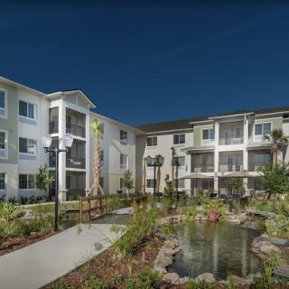 A modern apartment complex with landscaped gardens and a small pond.