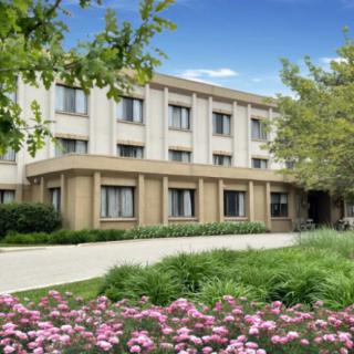 A three-story building surrounded by lush greenery and colorful flowers.