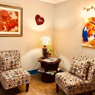 A cozy living room corner with patterned chairs, colorful artwork, and a warm lamp on a small table.