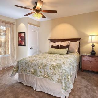A cozy bedroom with a floral bedspread, featuring a ceiling fan and soft lighting.