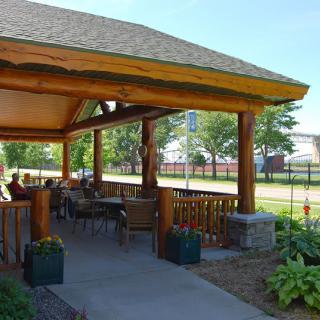 A cozy outdoor patio with wooden beams and seating, surrounded by a garden.