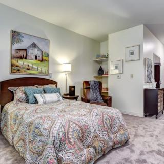 A cozy bedroom with a patterned bedspread, artwork on the walls, and a warm floor lamp.