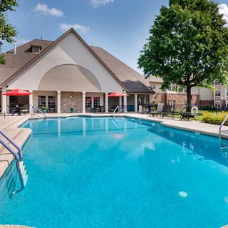 An outdoor swimming pool with a building and trees under a clear blue sky.