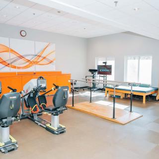 A modern fitness center with exercise equipment and a physical therapy area in a bright room.