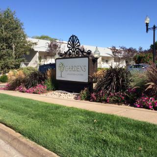 A landscaped area with a sign surrounded by grass and flowers, located near a large building.