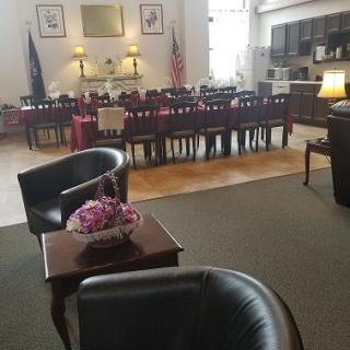 A cozy dining room with a large table, surrounded by leather chairs and decorated with flowers and lamps.