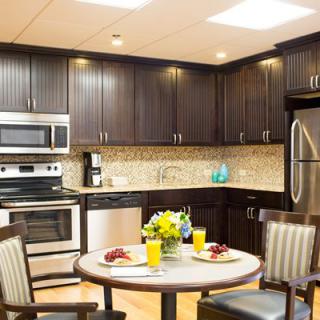 A modern kitchen with dark cabinets, stainless steel appliances, and a small dining table set for breakfast.