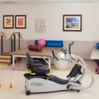 A rehabilitation room featuring exercise equipment, including an elliptical trainer and therapy tools.