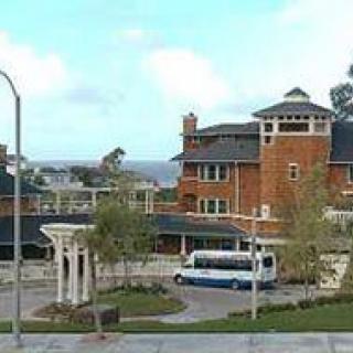 A scenic view of a brick building near the street with a bus parked in front and trees lining the area.