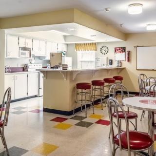 A retro-style diner kitchen with colorful flooring, counter stools, and tables.